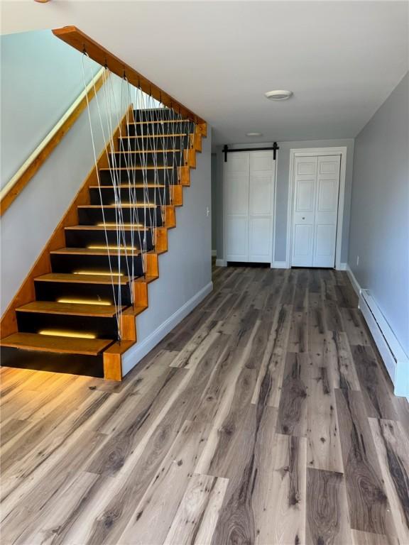 staircase featuring a barn door, a baseboard radiator, wood finished floors, and baseboards