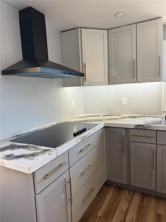 kitchen featuring black electric cooktop, gray cabinetry, wood finished floors, light countertops, and wall chimney exhaust hood