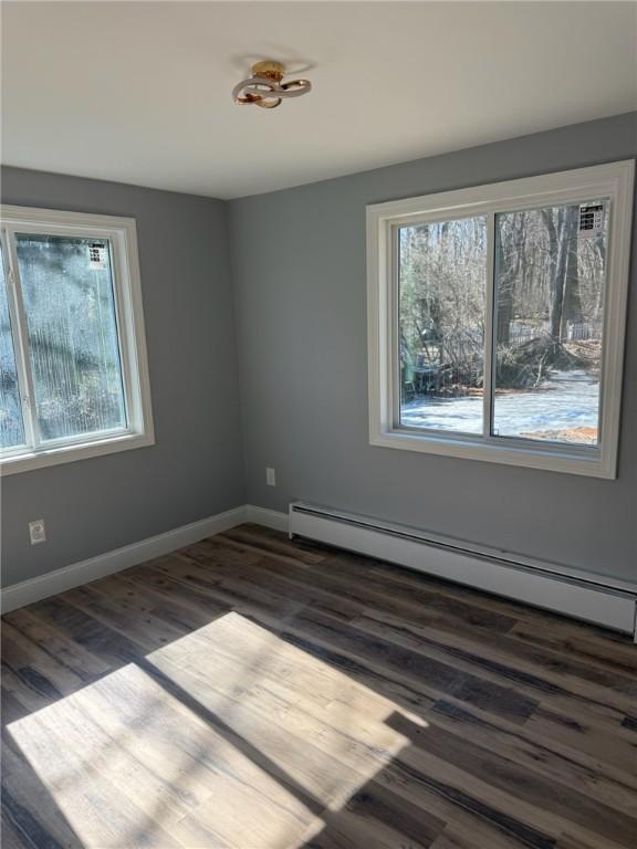 spare room with baseboards, plenty of natural light, a baseboard heating unit, and dark wood-type flooring