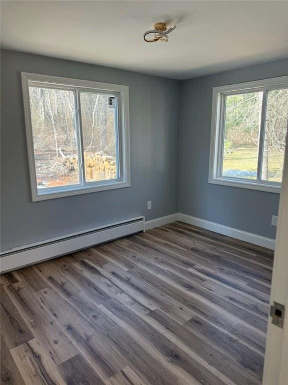 spare room featuring a baseboard heating unit, wood finished floors, and baseboards