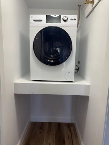 clothes washing area with stacked washer and dryer, baseboards, and wood finished floors