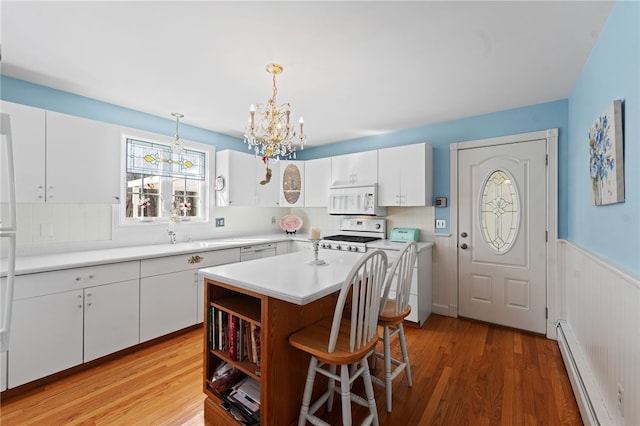 kitchen featuring a baseboard radiator, stove, white microwave, white cabinetry, and wainscoting