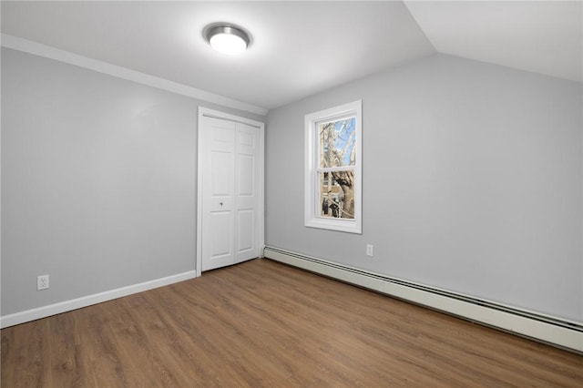 interior space featuring lofted ceiling, a closet, a baseboard heating unit, wood finished floors, and baseboards