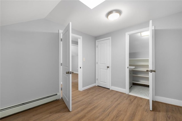 unfurnished bedroom featuring a baseboard radiator, vaulted ceiling, baseboards, and wood finished floors