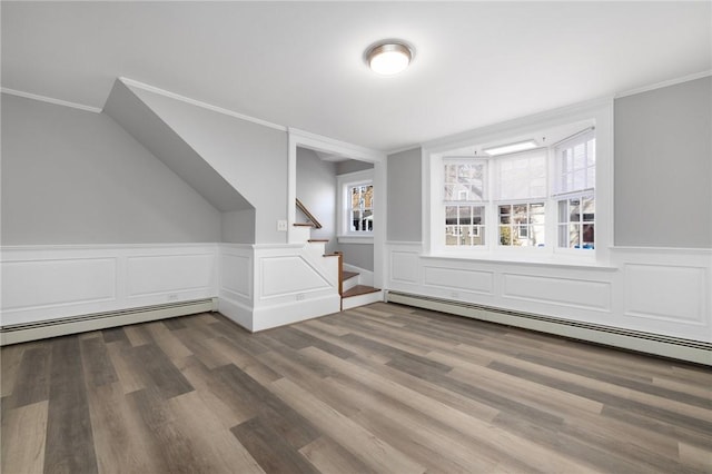 bonus room featuring a baseboard heating unit, wood finished floors, a wainscoted wall, and stairs