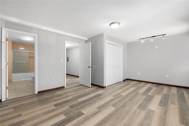 interior space with a closet, ensuite bath, wood finished floors, and baseboards