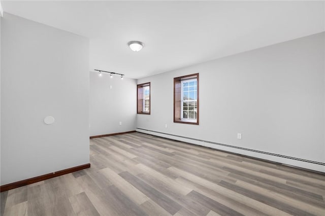 spare room featuring baseboards, a baseboard heating unit, and wood finished floors