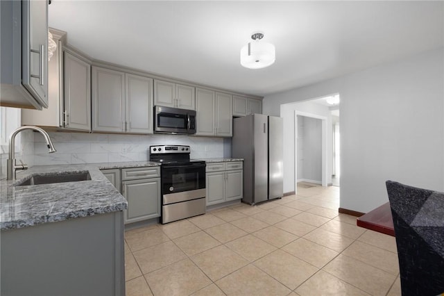 kitchen featuring light tile patterned floors, stainless steel appliances, tasteful backsplash, gray cabinetry, and a sink