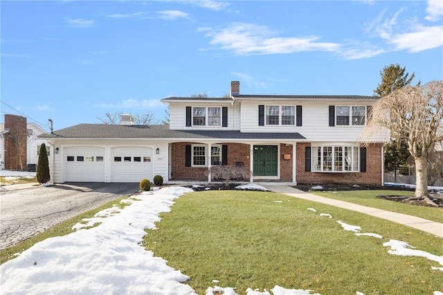 traditional home with aphalt driveway, brick siding, a chimney, a front yard, and a garage