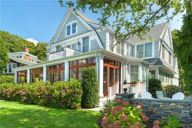 rear view of house featuring a yard, roof with shingles, and a sunroom