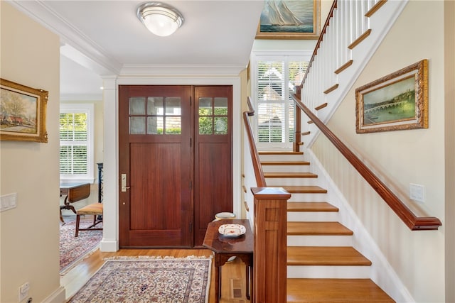 foyer entrance with decorative columns, baseboards, wood finished floors, stairs, and crown molding