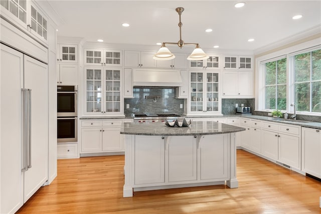 kitchen featuring stainless steel appliances, a sink, light wood-style floors, white cabinets, and custom exhaust hood