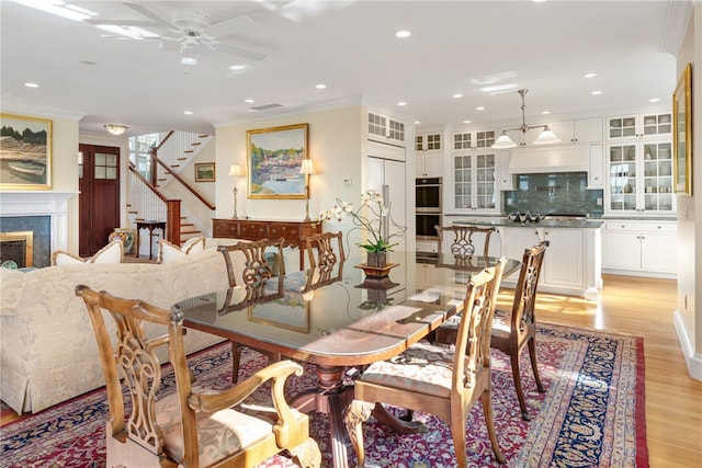 dining room with recessed lighting, a premium fireplace, ornamental molding, stairway, and light wood-type flooring