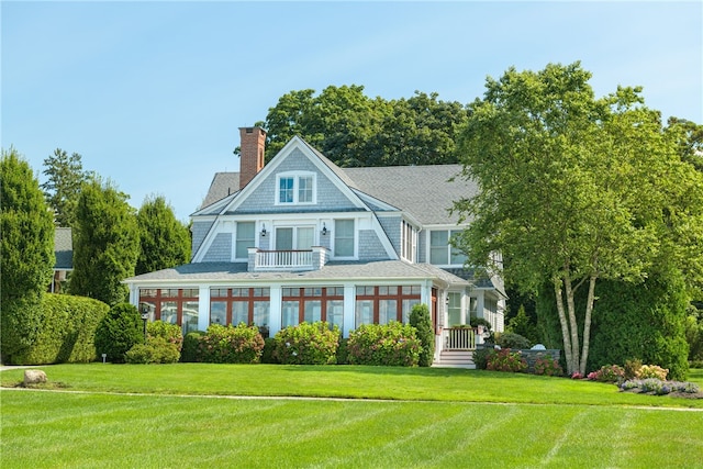 view of front of house featuring a chimney, a balcony, and a front lawn