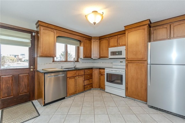 kitchen featuring stainless steel appliances, dark countertops, brown cabinets, and a sink