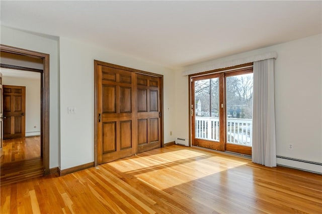 unfurnished bedroom featuring baseboards, light wood-type flooring, a baseboard radiator, and access to exterior