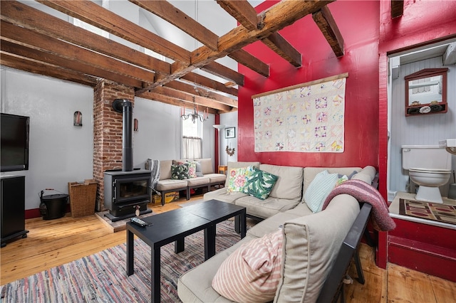 living room featuring beamed ceiling, wood-type flooring, and a wood stove