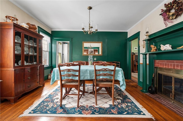 dining area with ornamental molding, a brick fireplace, wood finished floors, and an inviting chandelier