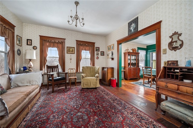 living area with wood-type flooring, an inviting chandelier, and wallpapered walls