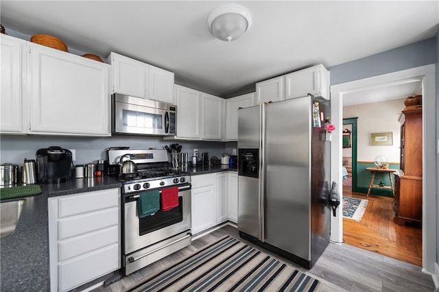 kitchen featuring appliances with stainless steel finishes, dark countertops, wood finished floors, and white cabinets