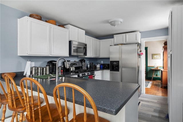 kitchen featuring dark countertops, appliances with stainless steel finishes, a peninsula, light wood-style floors, and white cabinetry