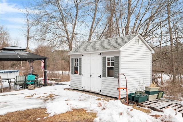 snow covered structure with an outdoor structure, a gazebo, and a shed