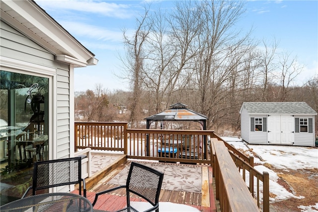 snow covered deck featuring a storage shed, a gazebo, and an outbuilding