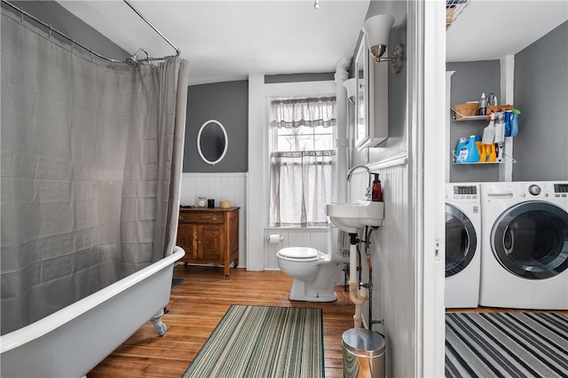 bathroom featuring wainscoting, toilet, wood finished floors, washing machine and dryer, and a sink