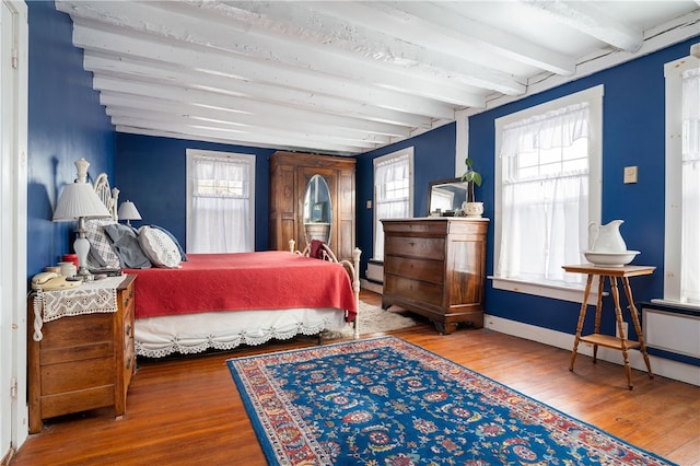 bedroom with a baseboard radiator, beam ceiling, baseboards, and wood finished floors