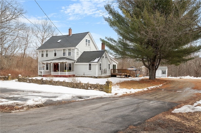 view of front of property featuring covered porch, a deck, and a chimney