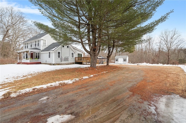 view of snow covered exterior featuring driveway, an outdoor structure, a deck, and a storage shed