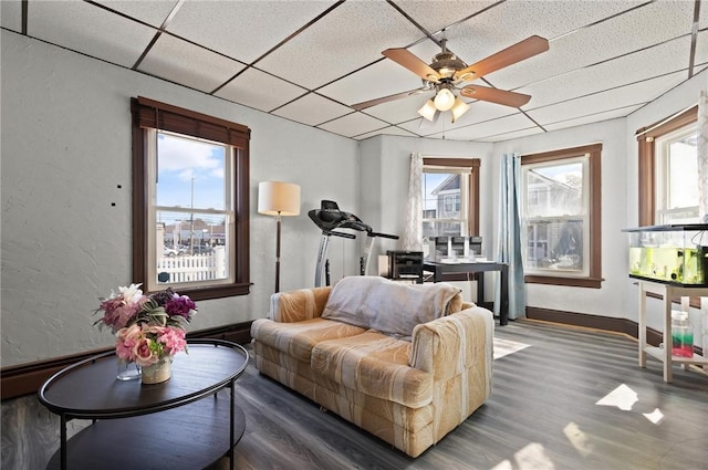 sitting room with baseboards, a ceiling fan, a textured wall, a drop ceiling, and wood finished floors