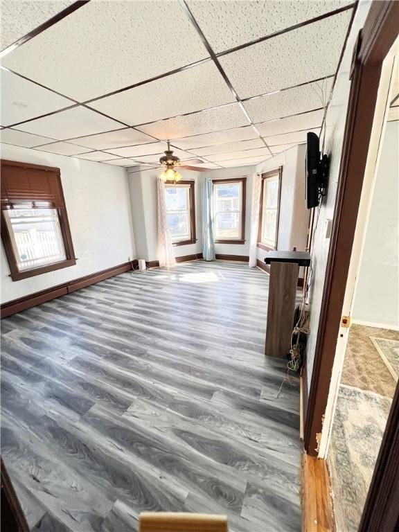 interior space with ceiling fan, wood finished floors, a paneled ceiling, and baseboards