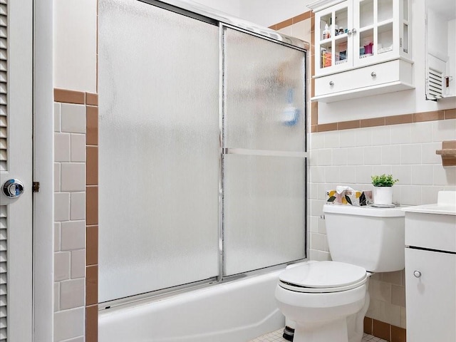 full bathroom with toilet, bath / shower combo with glass door, vanity, tile walls, and tile patterned floors