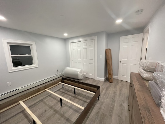 bedroom featuring a baseboard heating unit, a closet, wood finished floors, and recessed lighting