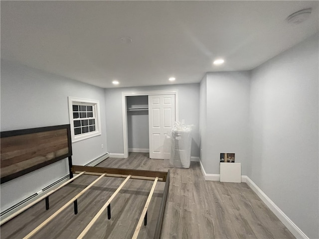 unfurnished bedroom featuring a baseboard heating unit, recessed lighting, baseboards, and wood finished floors