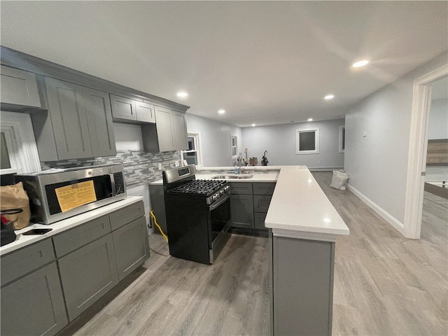 kitchen featuring stainless steel appliances, backsplash, gray cabinetry, a sink, and a peninsula