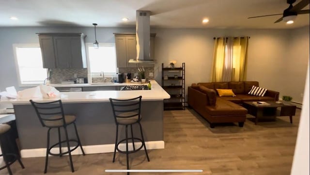 kitchen featuring decorative backsplash, a breakfast bar, island exhaust hood, light countertops, and a sink