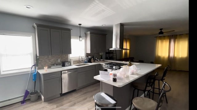 kitchen featuring a baseboard radiator, gray cabinetry, a peninsula, wall chimney range hood, and appliances with stainless steel finishes