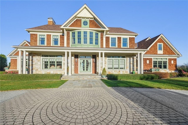 view of front facade featuring stone siding, a chimney, covered porch, french doors, and a front lawn