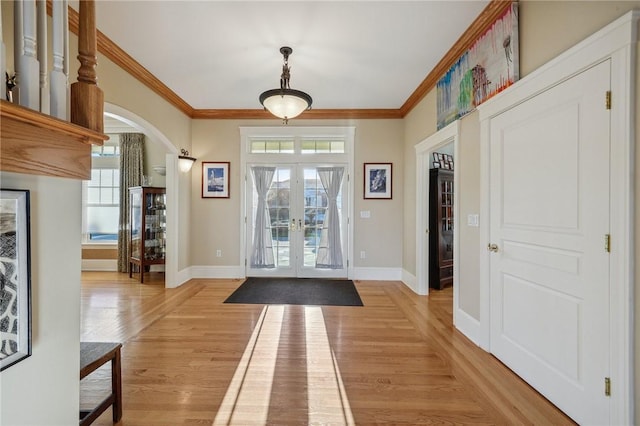 entryway with arched walkways, french doors, crown molding, light wood-style floors, and baseboards