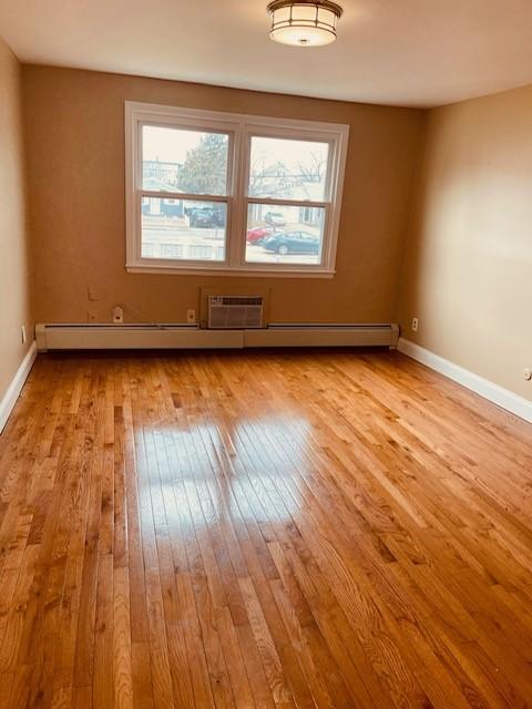 unfurnished room with wood-type flooring, baseboards, and an AC wall unit