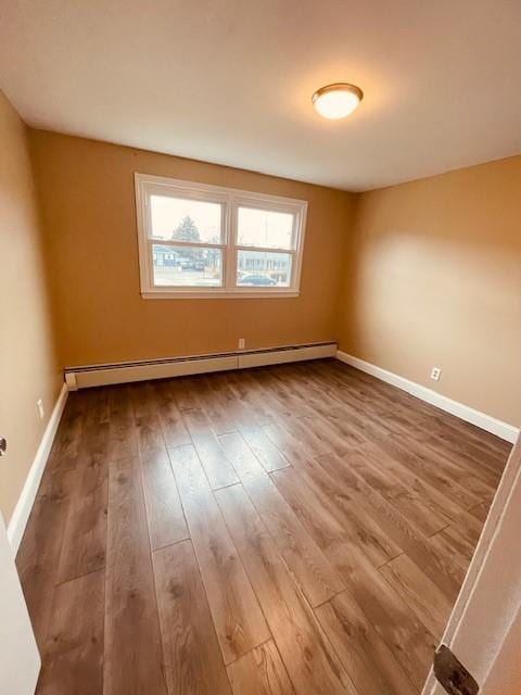 unfurnished room featuring a baseboard radiator, wood finished floors, and baseboards