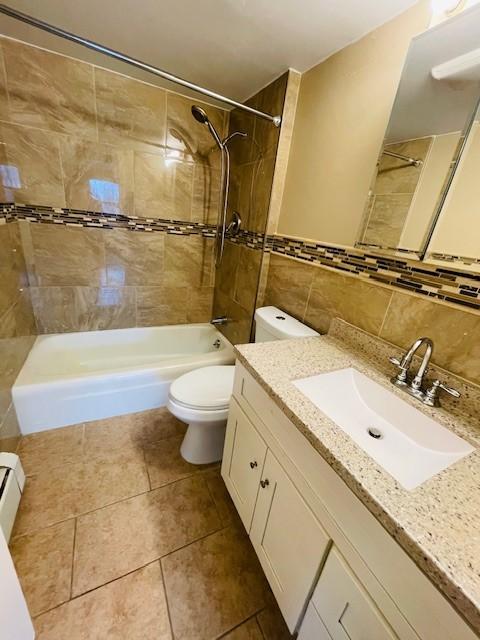 full bath with tile walls, toilet, a baseboard heating unit, washtub / shower combination, and tile patterned floors