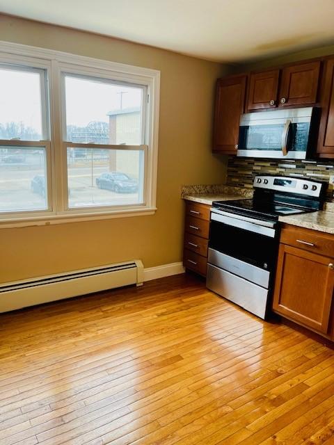 kitchen with tasteful backsplash, baseboards, a baseboard radiator, appliances with stainless steel finishes, and light wood-style floors