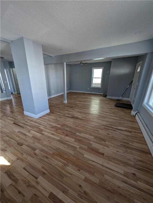 below grade area featuring a baseboard radiator, wood finished floors, baseboards, and a textured ceiling