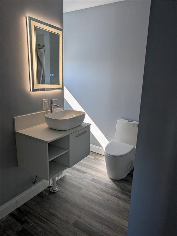 bathroom featuring baseboards, vanity, toilet, and wood finished floors