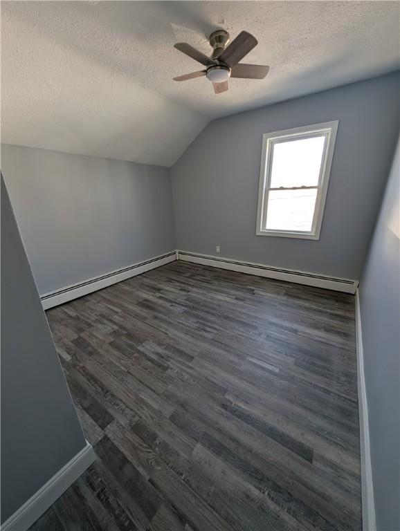 additional living space with baseboards, a ceiling fan, dark wood-style flooring, vaulted ceiling, and a textured ceiling