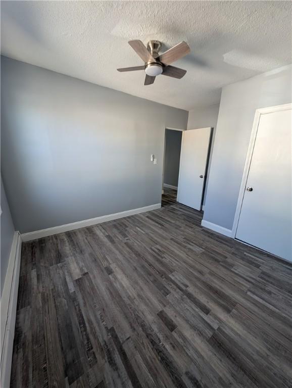 unfurnished bedroom with a baseboard radiator, baseboards, dark wood finished floors, and a textured ceiling