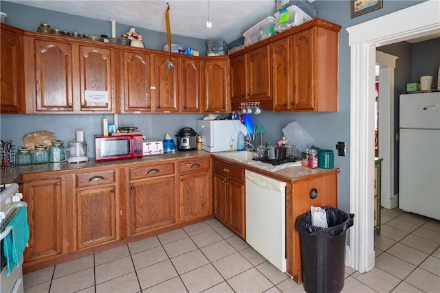 kitchen with white appliances, light tile patterned flooring, a sink, and brown cabinets